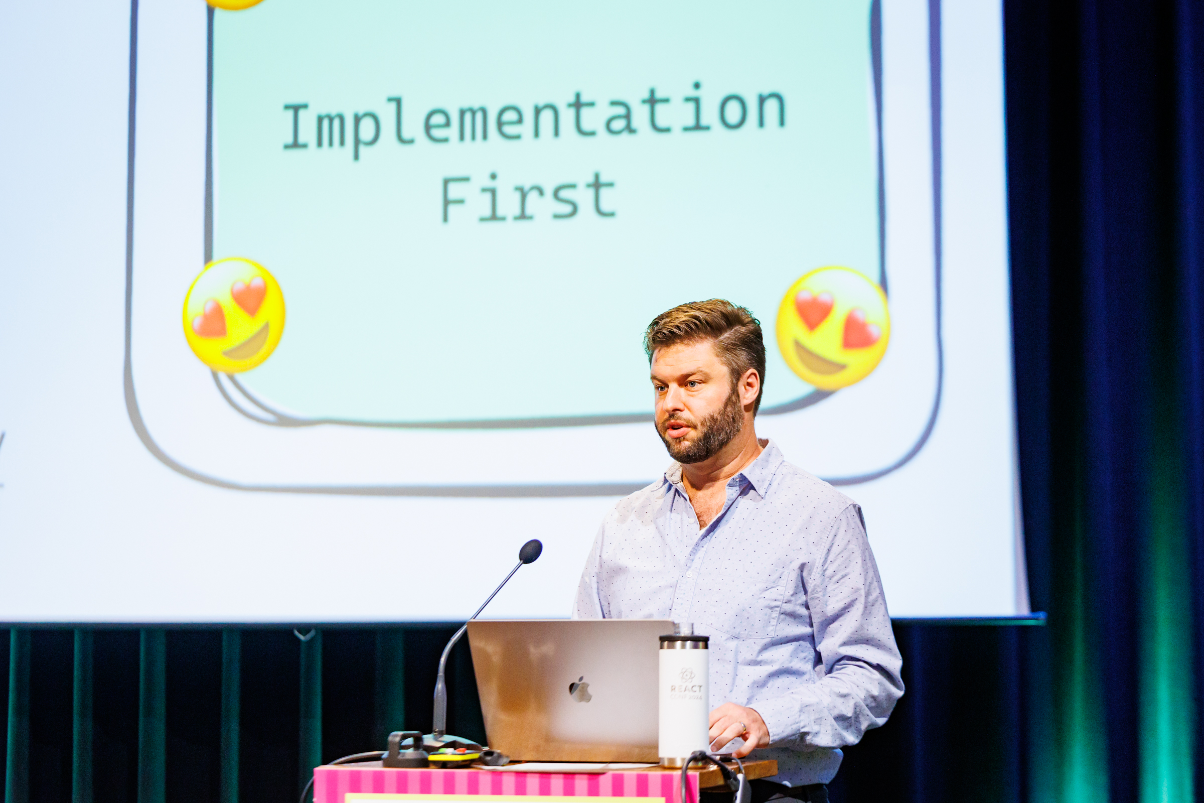 Jordan on stage with a slide showing his love of implementation first GraphQL shown behind him.
